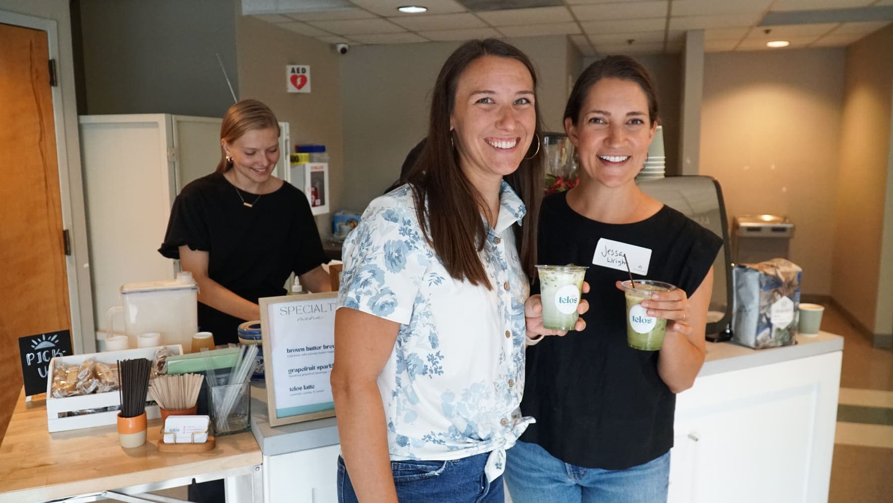 Two guests smiling as they hold drinks beside the Telos Coffee cart