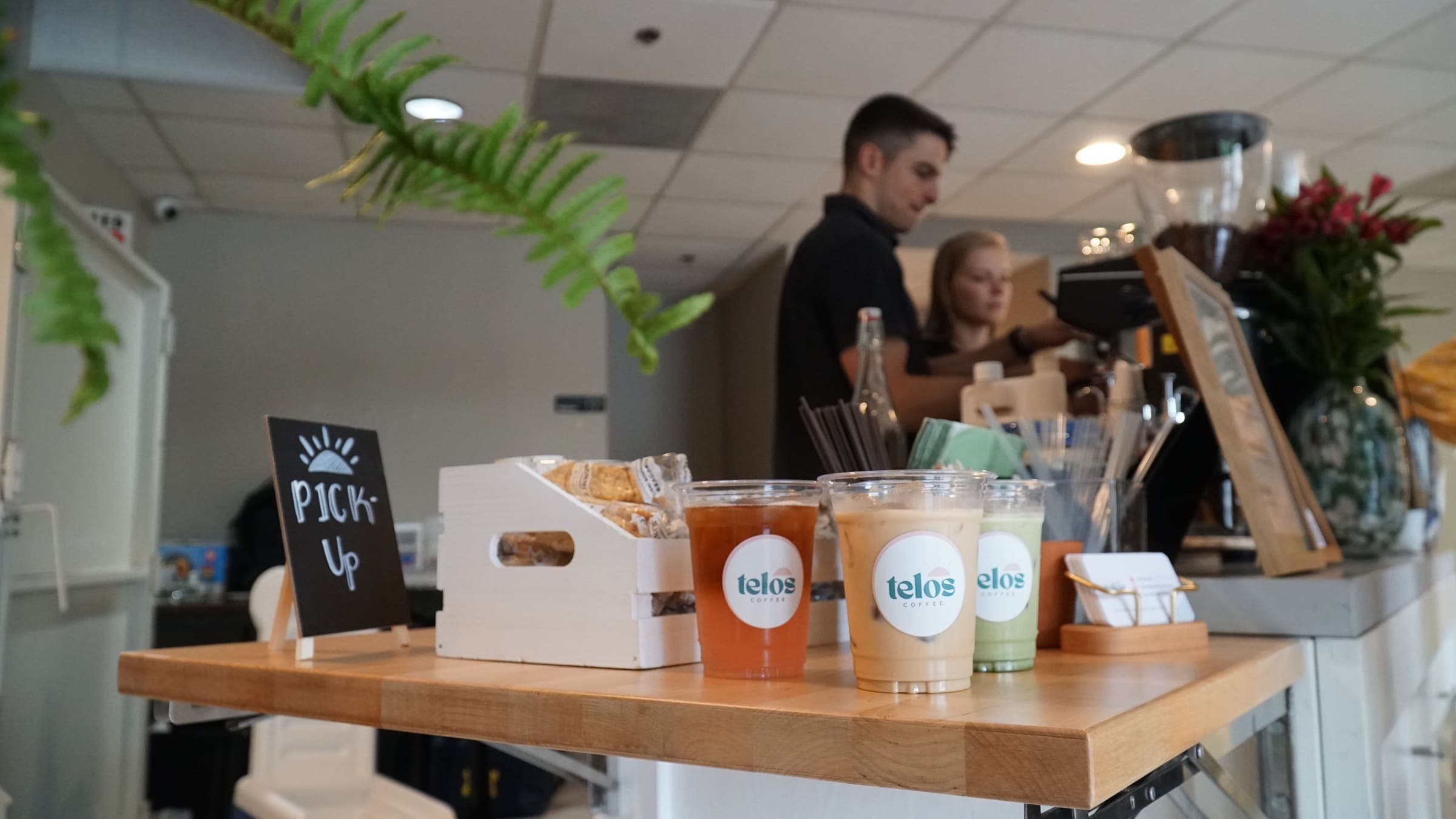 Branded Telos Coffee drinks lined up on the pickup counter while baristas work behind the cart